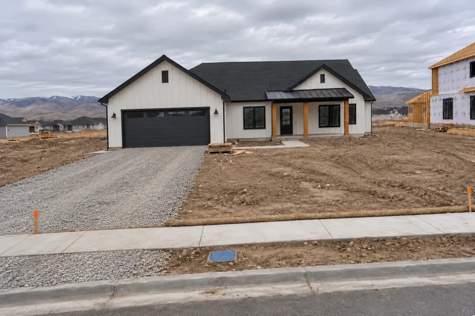 New single-story farmhouse on closing day with a gravel driveway base, bare graded soil, a straw wattle along the sidewalk, and survey stakes at the front corners.