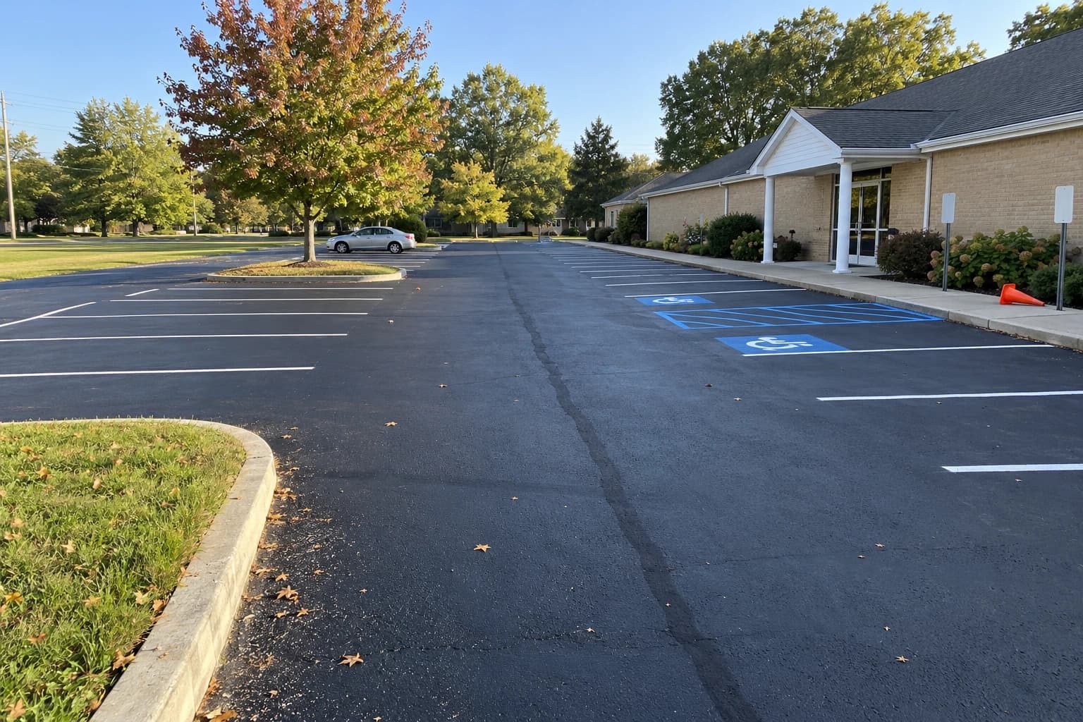 The church parking lot after sealcoating and restriping, seen from the walk by the building: dark fresh sealer, white stall lines, a tree island and the blue accessible aisle by the doors